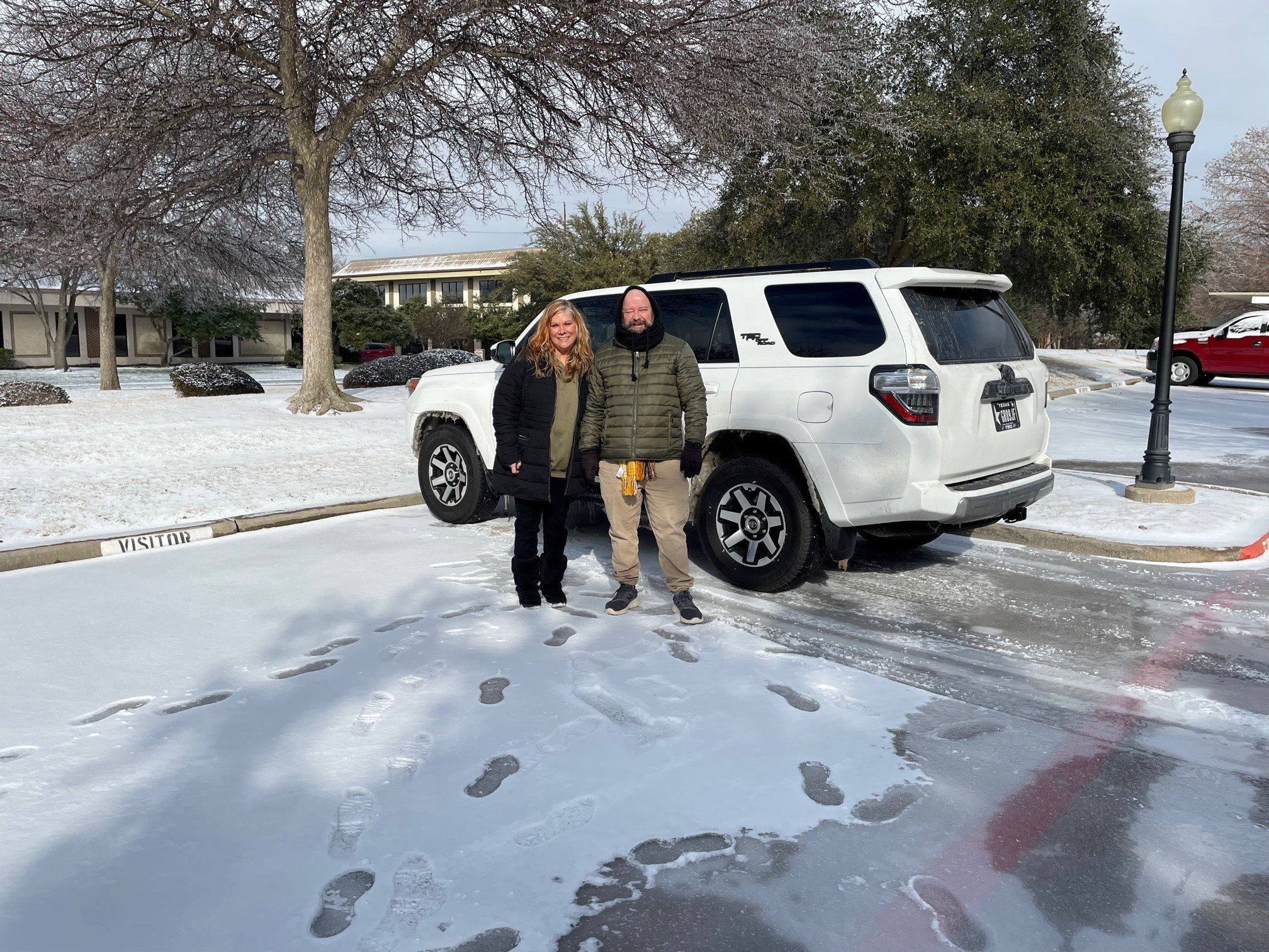 two staff members smile in front of a snow-covered car