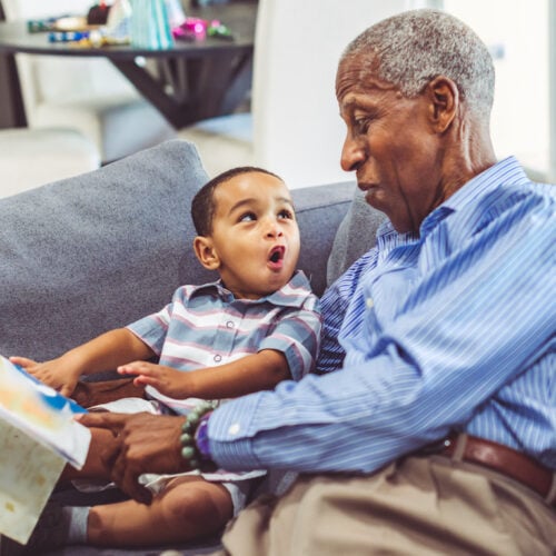 Older man reading to his grandson on the couch