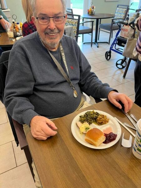 senior man smiles while sitting at a table with his Thanksgiving meal