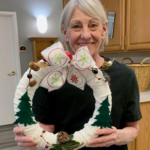 senior woman smiles while holding her homemade Christmas wreath