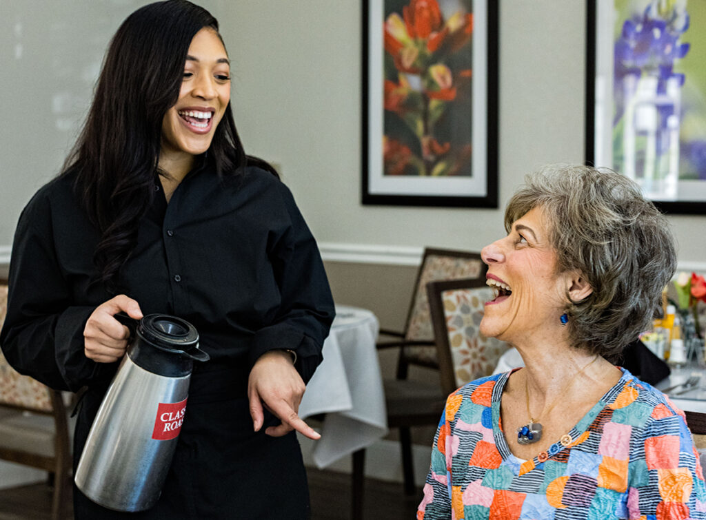 Senior woman thriving in an assisted living community as she laughs with a caregiver pouring her a drink